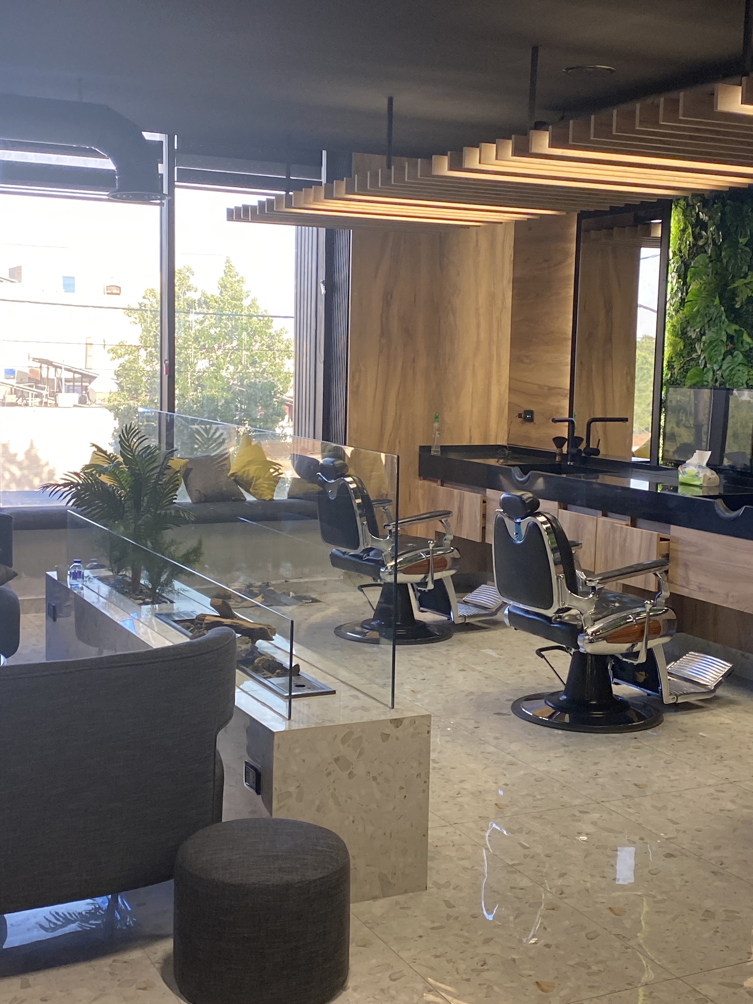 Chrome barber chairs beside a black marble sink counter and floor-to-ceiling windows